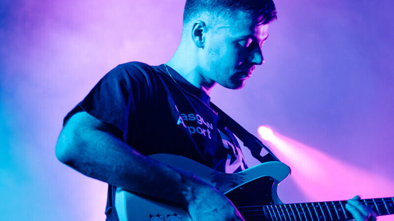 Billede af en musiker der spiller guitar på en scene med formstøbte musikørepropper.
