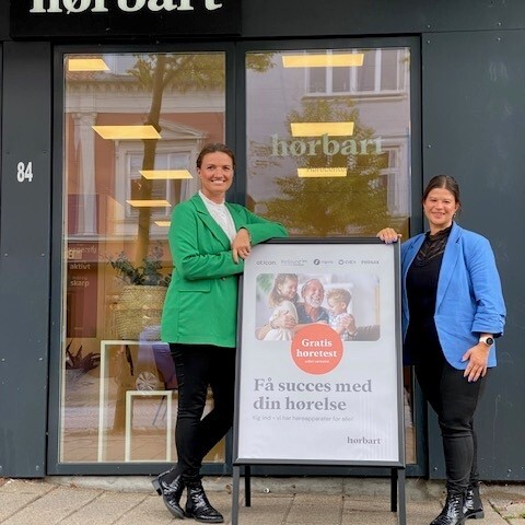 Indehaver Stinne Møller Nordby og medarbejder Tina Hillerup står foran Hørbarts klinik i Skanderborg ved et skilt med information om gratis høretest.